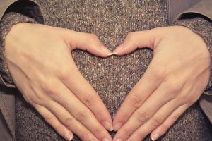 woman's hands held in heart shape over pregnant belly